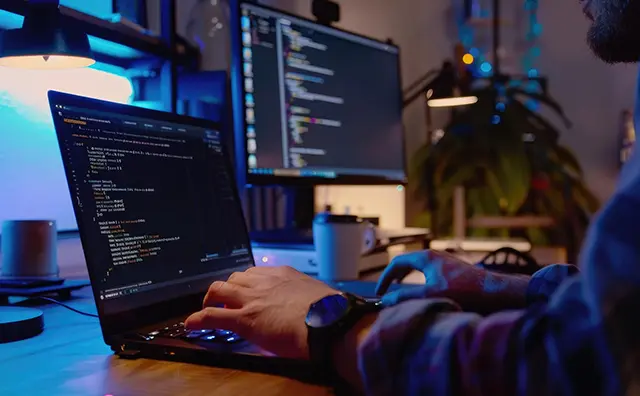 Programmer coding at a desk with multiple screens, highlighting digital infrastructure.