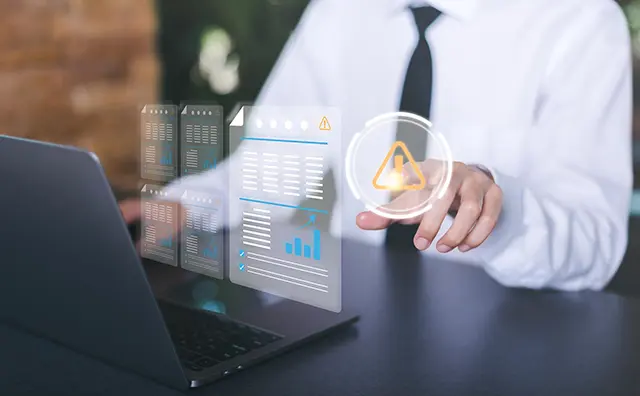 Data analyst addresses warning signs within a digital infrastructure on a laptop.