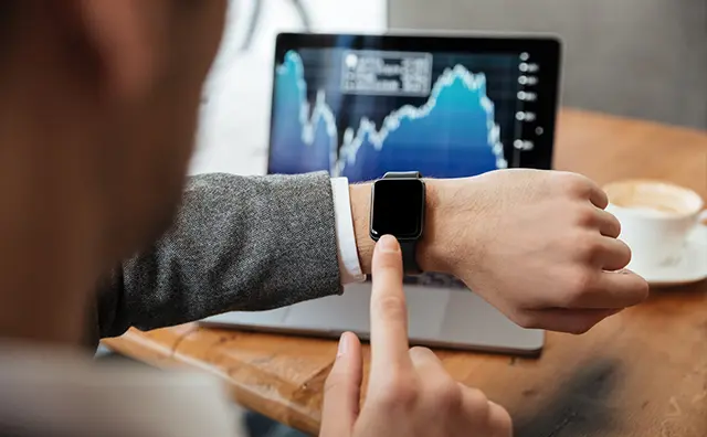 Man interacts with a smartwatch, accessing fintech data displayed on a laptop.