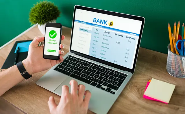 Person uses laptop and smartphone for mobile banking, showing fintech in action.